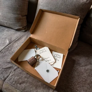 Caja de cartón abierta sobre un sofá con sobres cerrados, un candado y papeles con pistas escritas a mano. Preparación de un escape room casero con materiales sencillos.
